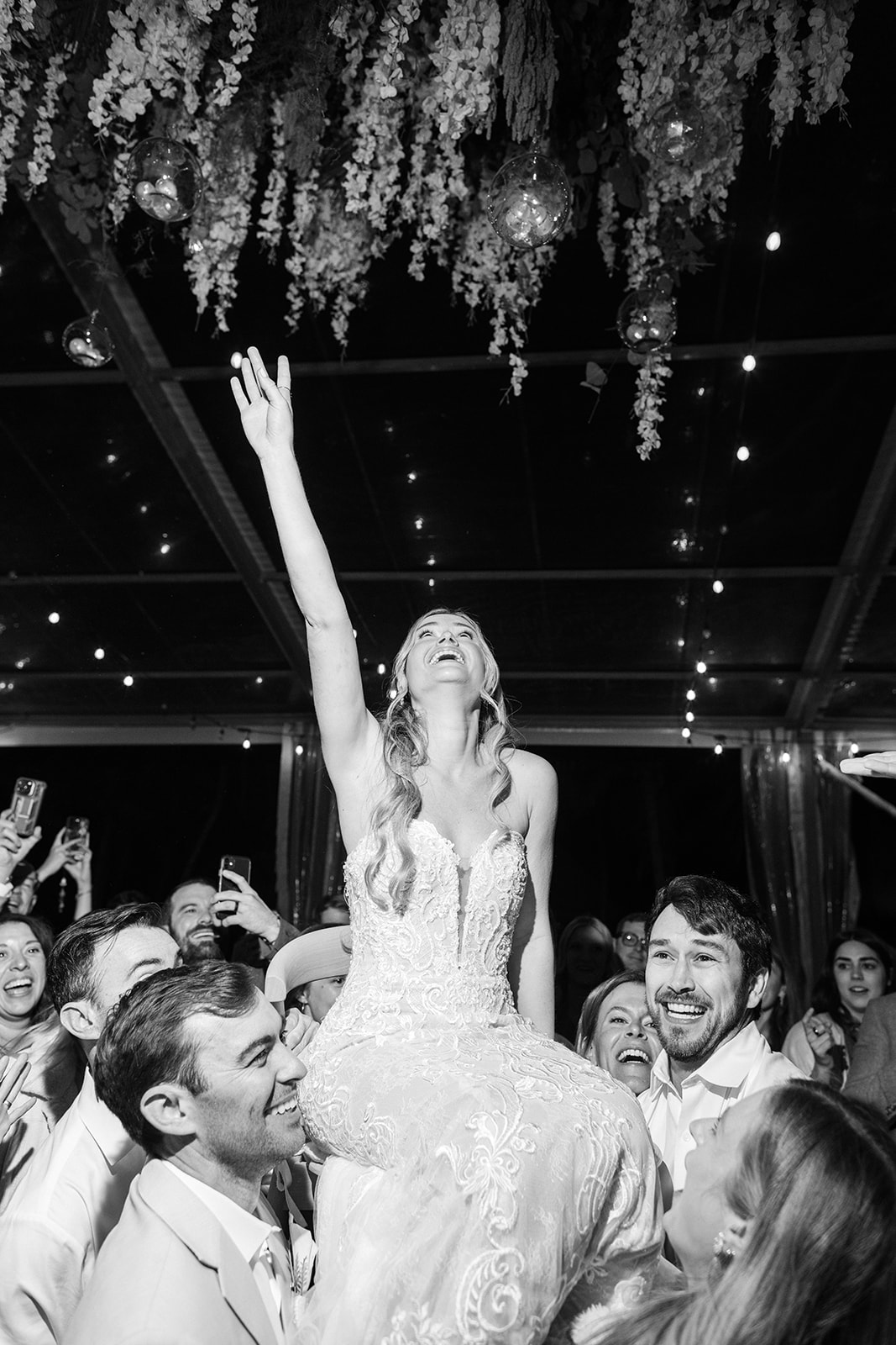 Bride dancing at reception under string lights, black and white